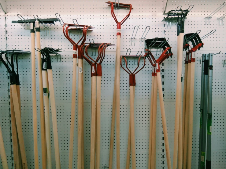 several red shovels hanging on the wall above some metal pegs