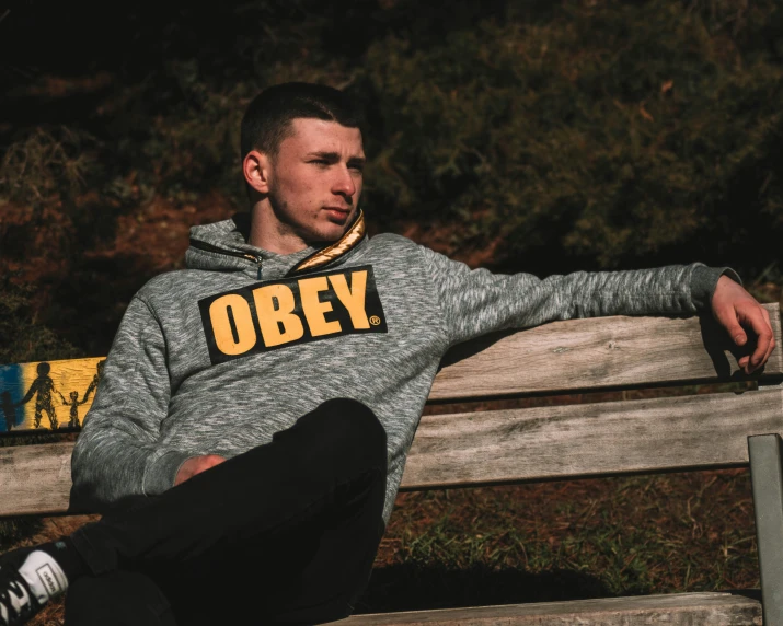 a man sitting on a park bench wearing a obey sweatshirt