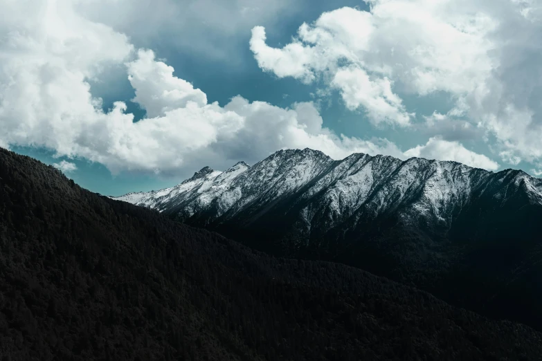 the mountain range with snow on top and clouds moving through