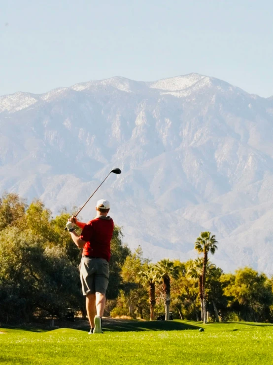 man in red jacket playing golf on a green course