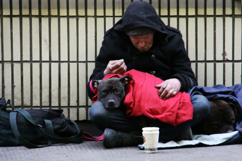 man sitting on the ground with his dog wearing a coat