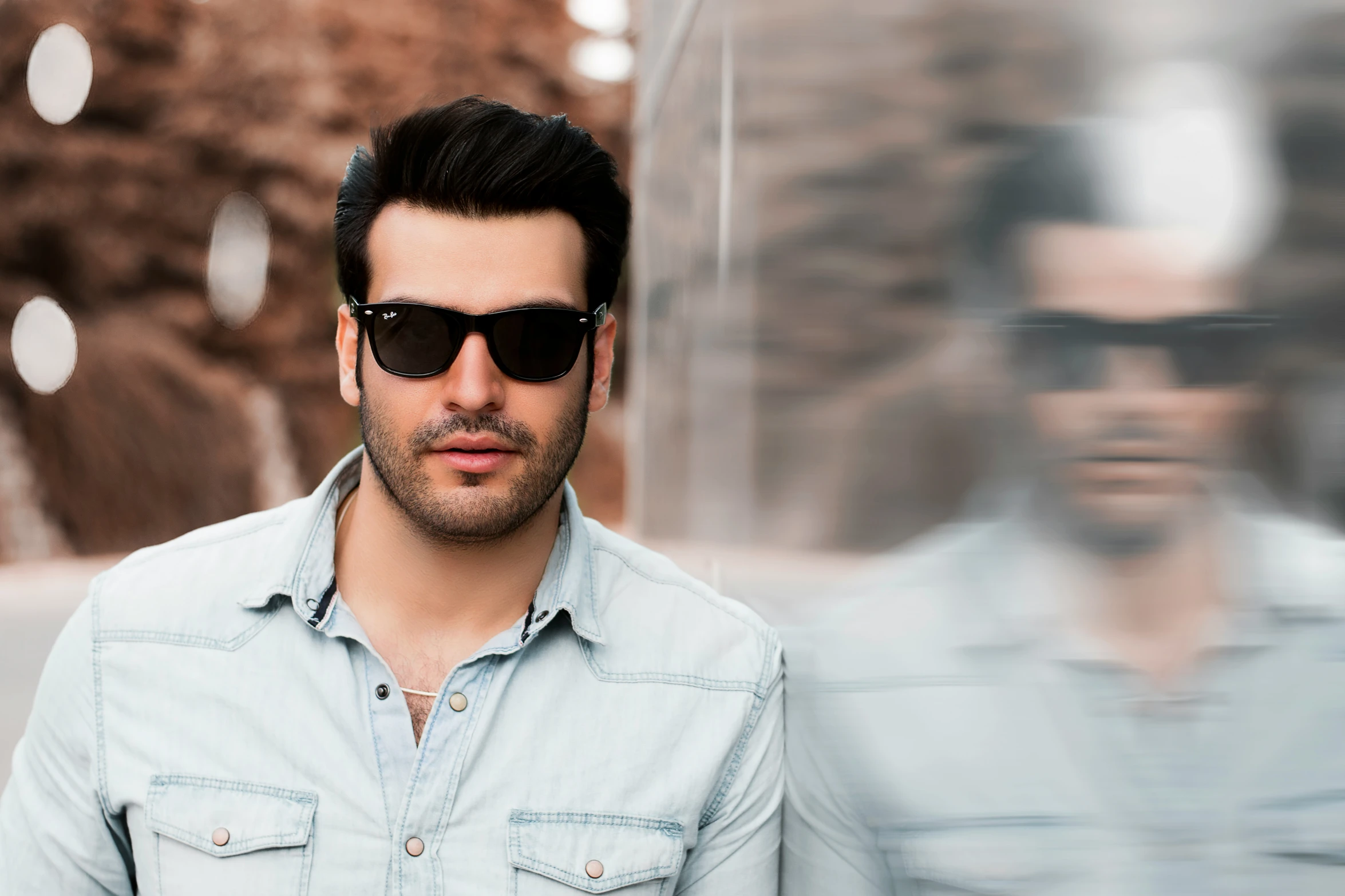 a man is wearing shades as he stands in front of a large rock wall