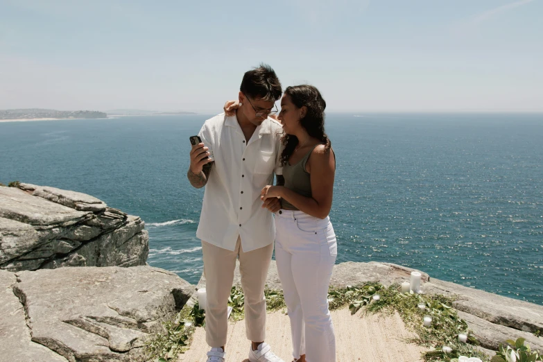 two young people at the top of a cliff near the ocean