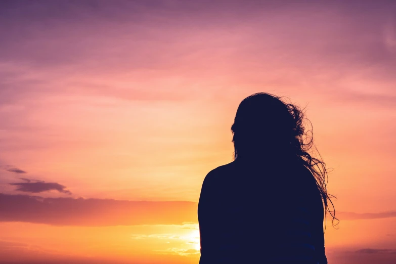 a person with long hair is watching the sunset