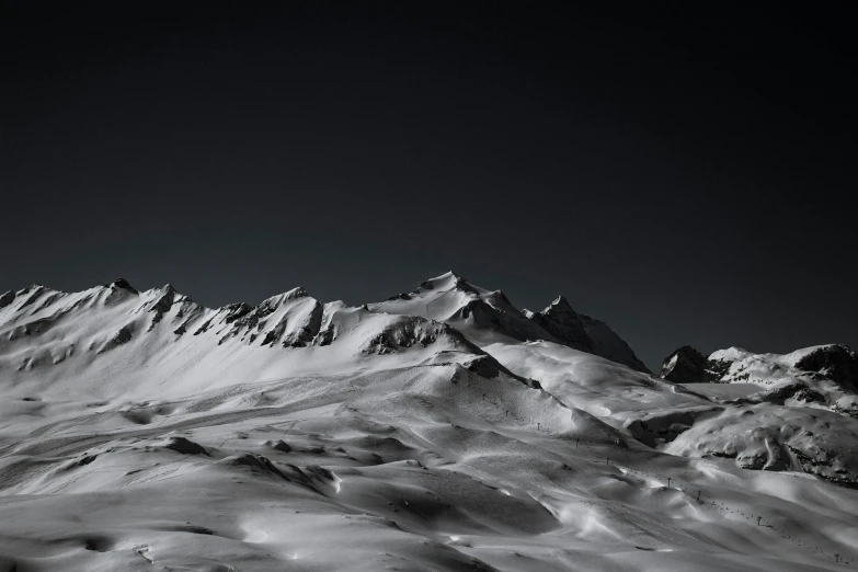 the top of some snow covered mountains under a dark sky