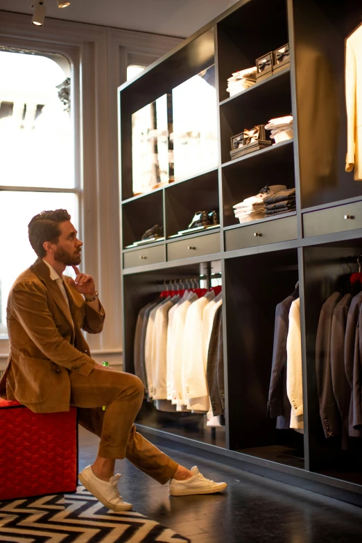 the man is sitting on a suitcase and looking into his closet