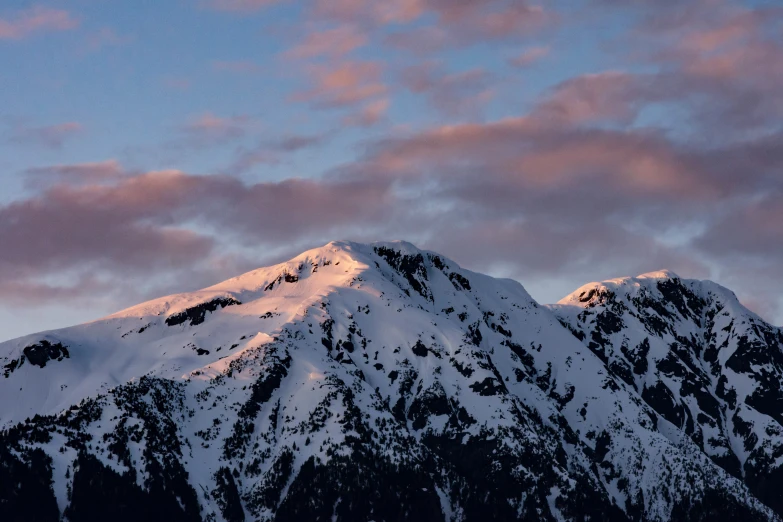 a large snow covered mountain with pink clouds in the background