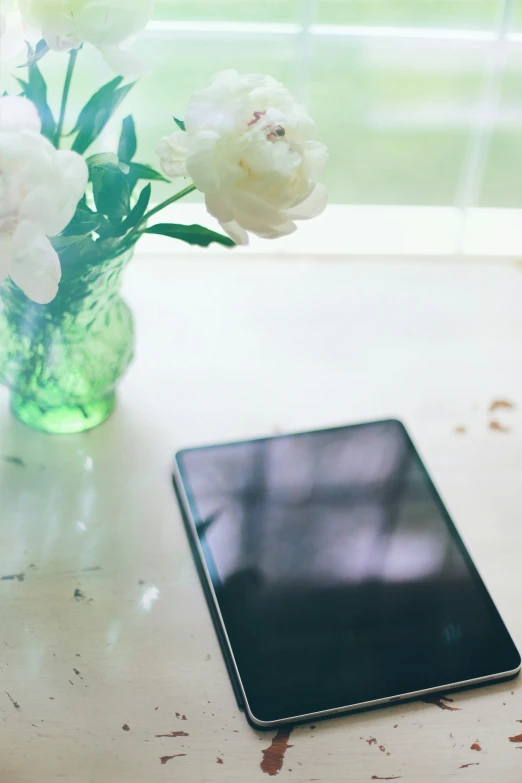 a tablet sits on a table with flowers in a vase