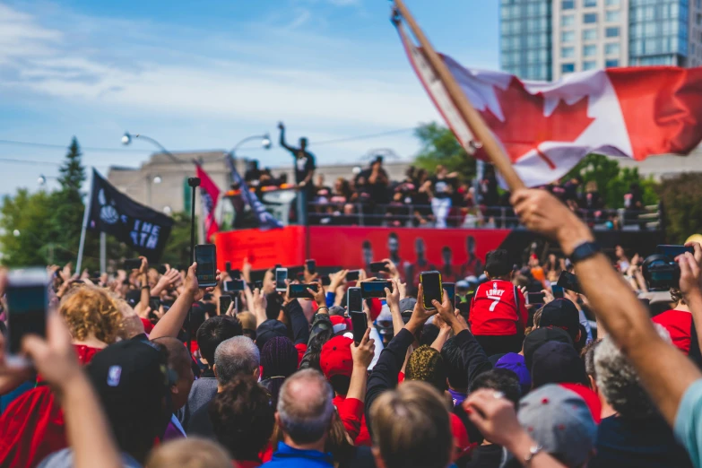 a large crowd holds up a canada flag as they watch an outdoor ceremony