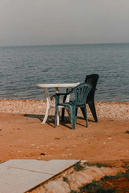 a table and chairs sit on the beach shore near the water