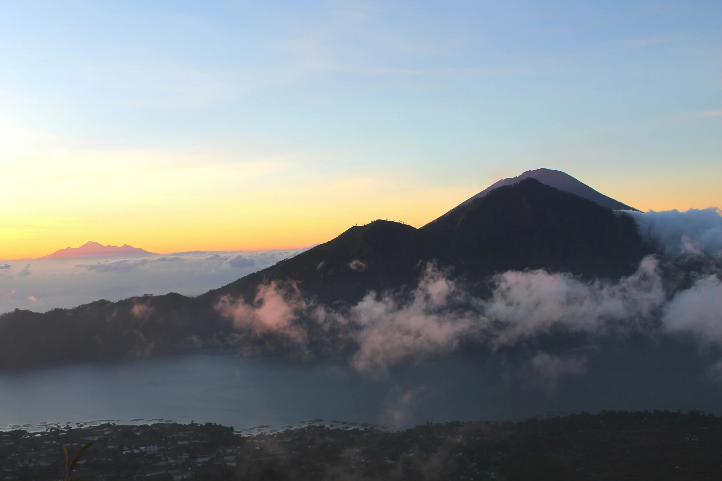 a small mountain above a body of water at sunset