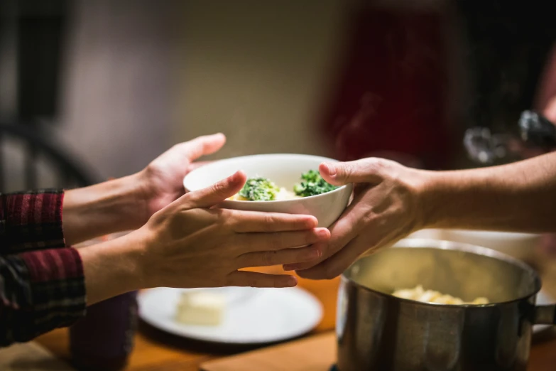 two hands holding a bowl of food over a table