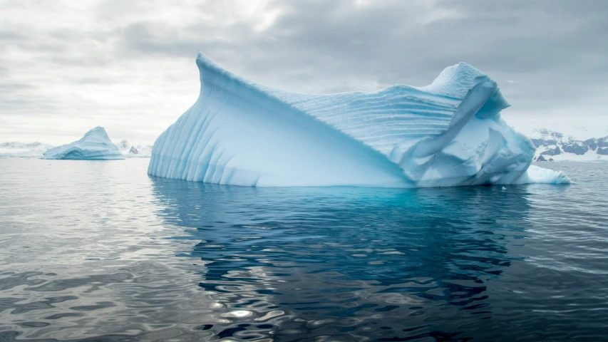 an iceberg floating in the ocean on a cloudy day