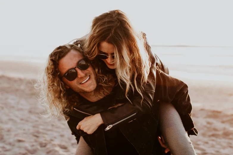 a man carrying a woman while she's walking along the beach