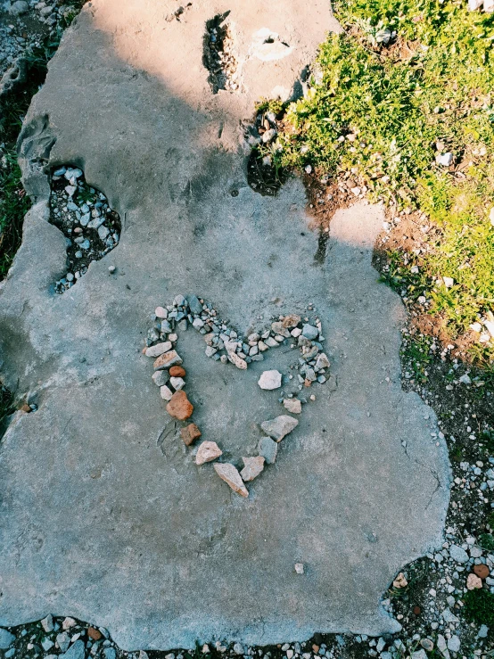 a rock heart sitting in a gravel path near green grass