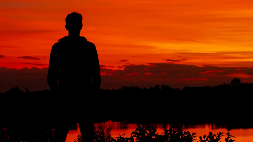 a man standing at the edge of a lake at sunset