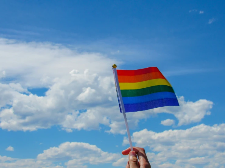 a person's hand holds a rainbow flag in the blue sky