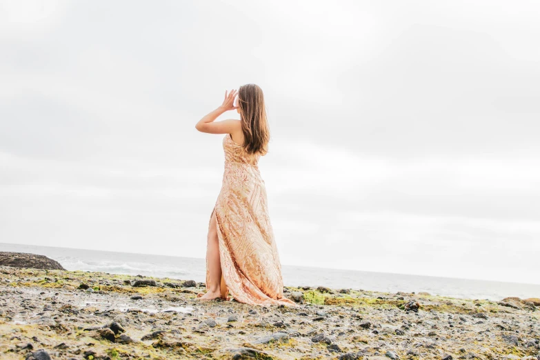 an attractive young woman standing on top of a rocky beach