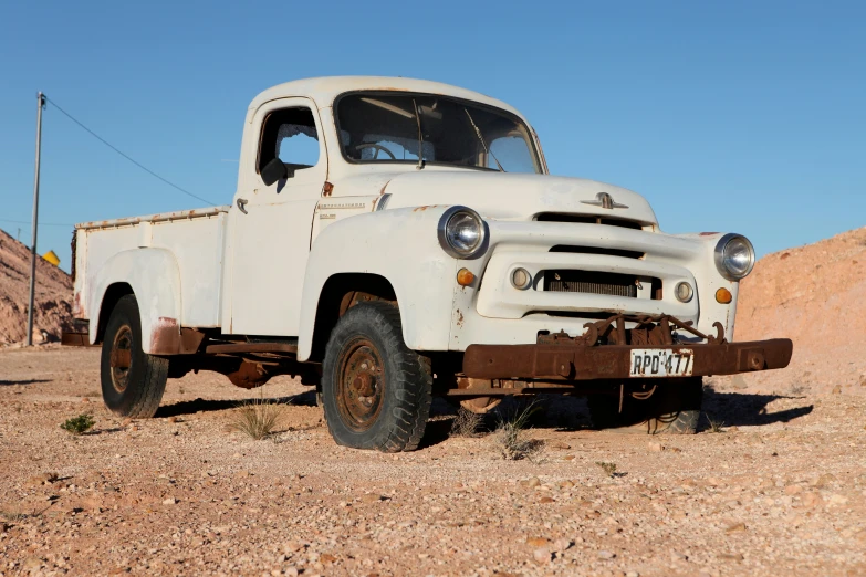 an old truck parked on the dirt near sand hills