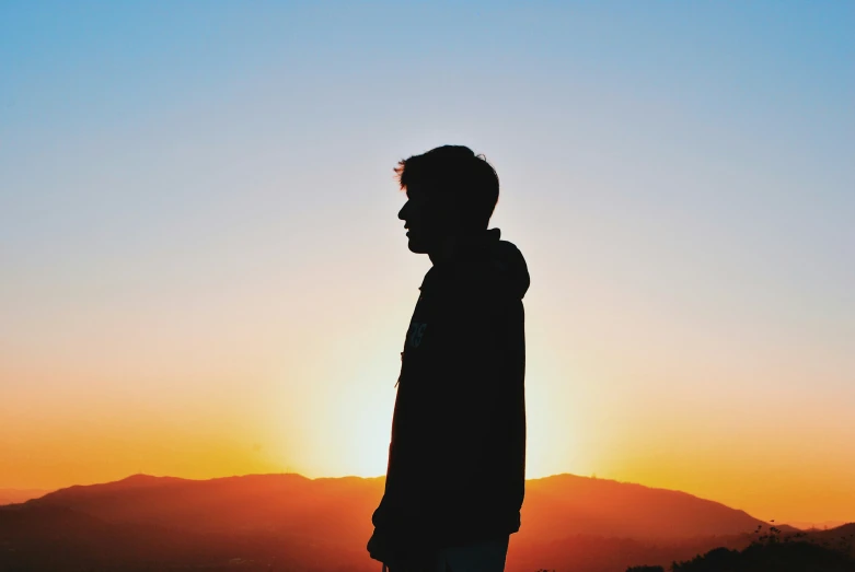 a man standing alone in front of a sunset
