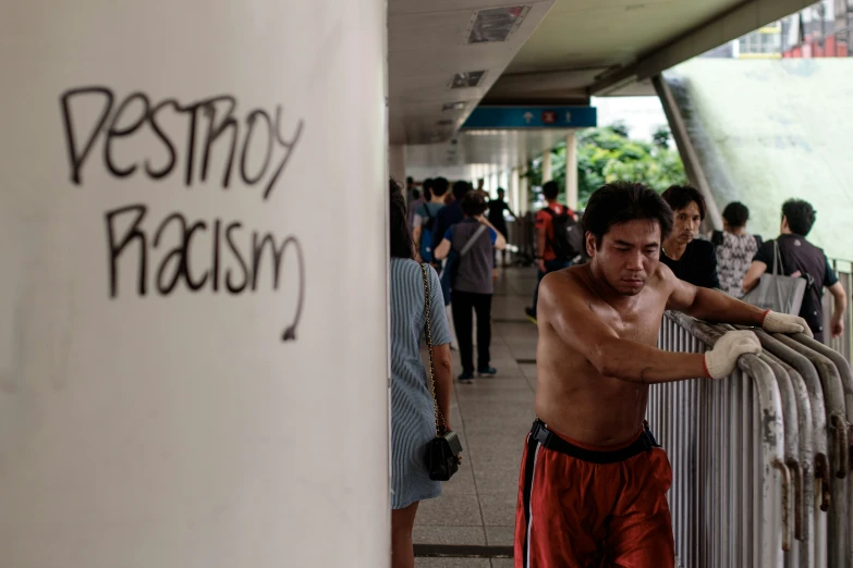 a shirtless man stands next to a rail with words written on it