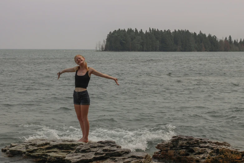 a woman is standing on the edge of a cliff in front of a large body of water