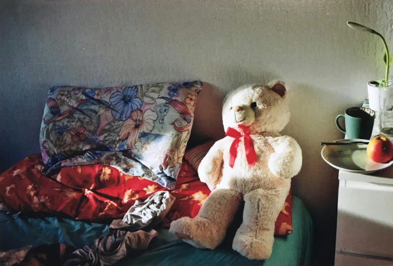 a teddy bear sits on a bed with red pillows