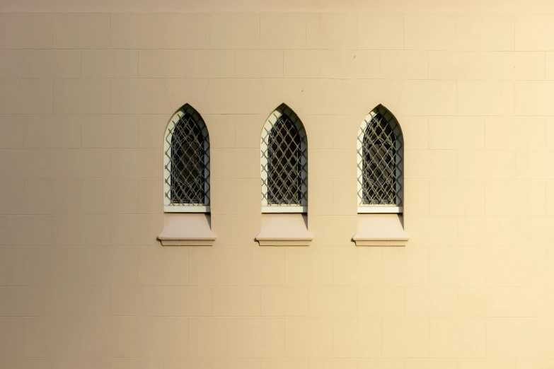 three arched windows on a cream colored brick wall