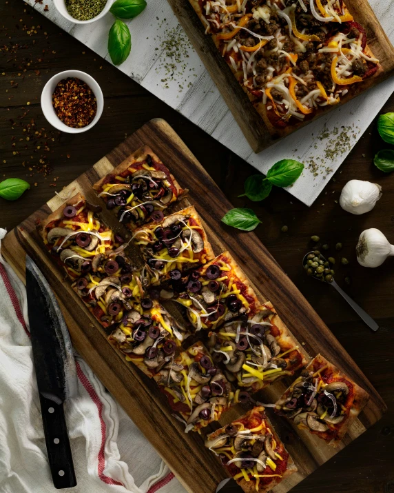 two square pizzas on a wooden  board with different toppings