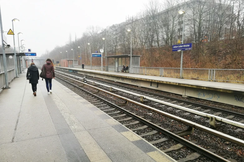 two people walking on a platform with the railway tracks