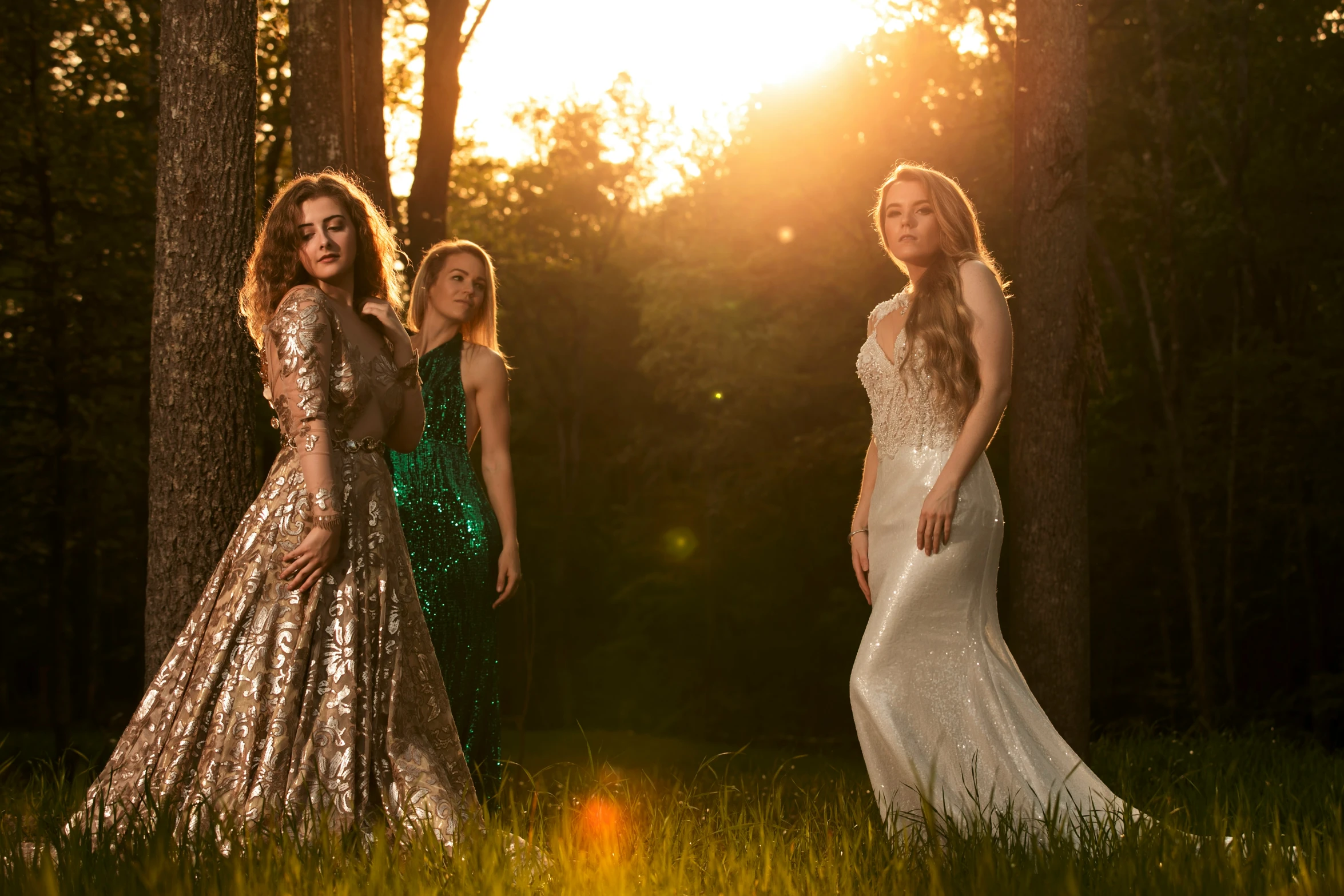 three beautiful women stand in the grass, in front of a tree