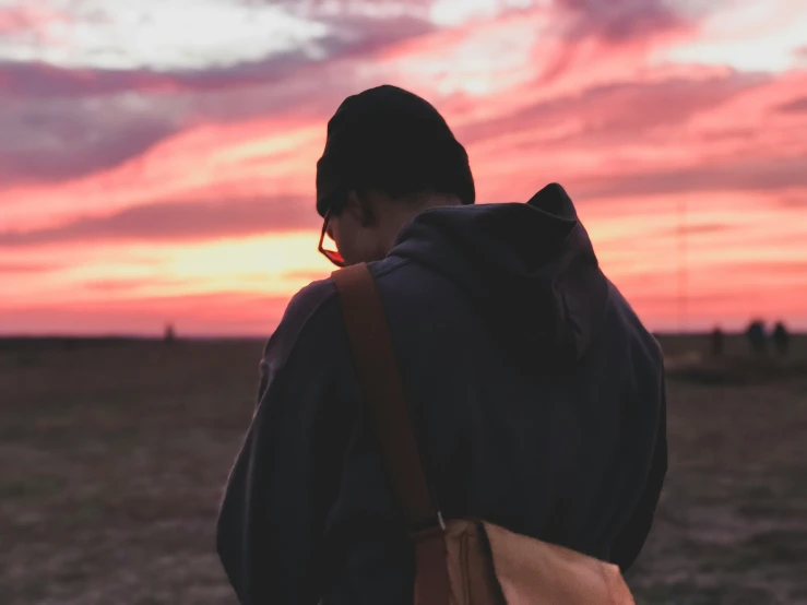 the back of a person walking in a field at sunset