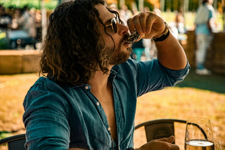 a man in blue shirt and glasses sitting at table with wine