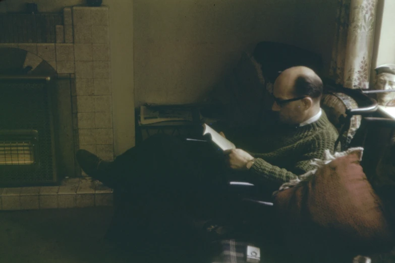 a man reading a book with another man sitting on a couch