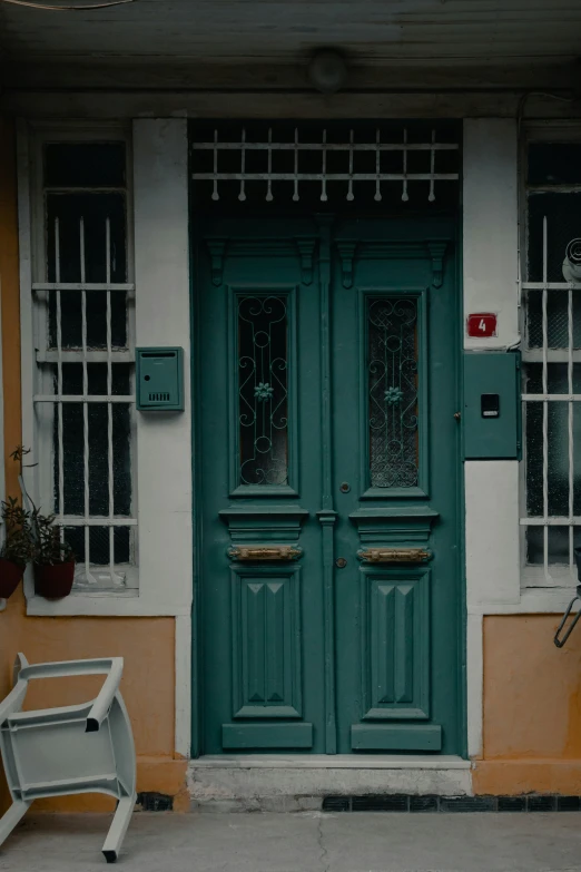 a green door sits next to two white chairs on the side walk