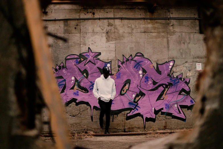 a man in white standing by graffiti on the wall