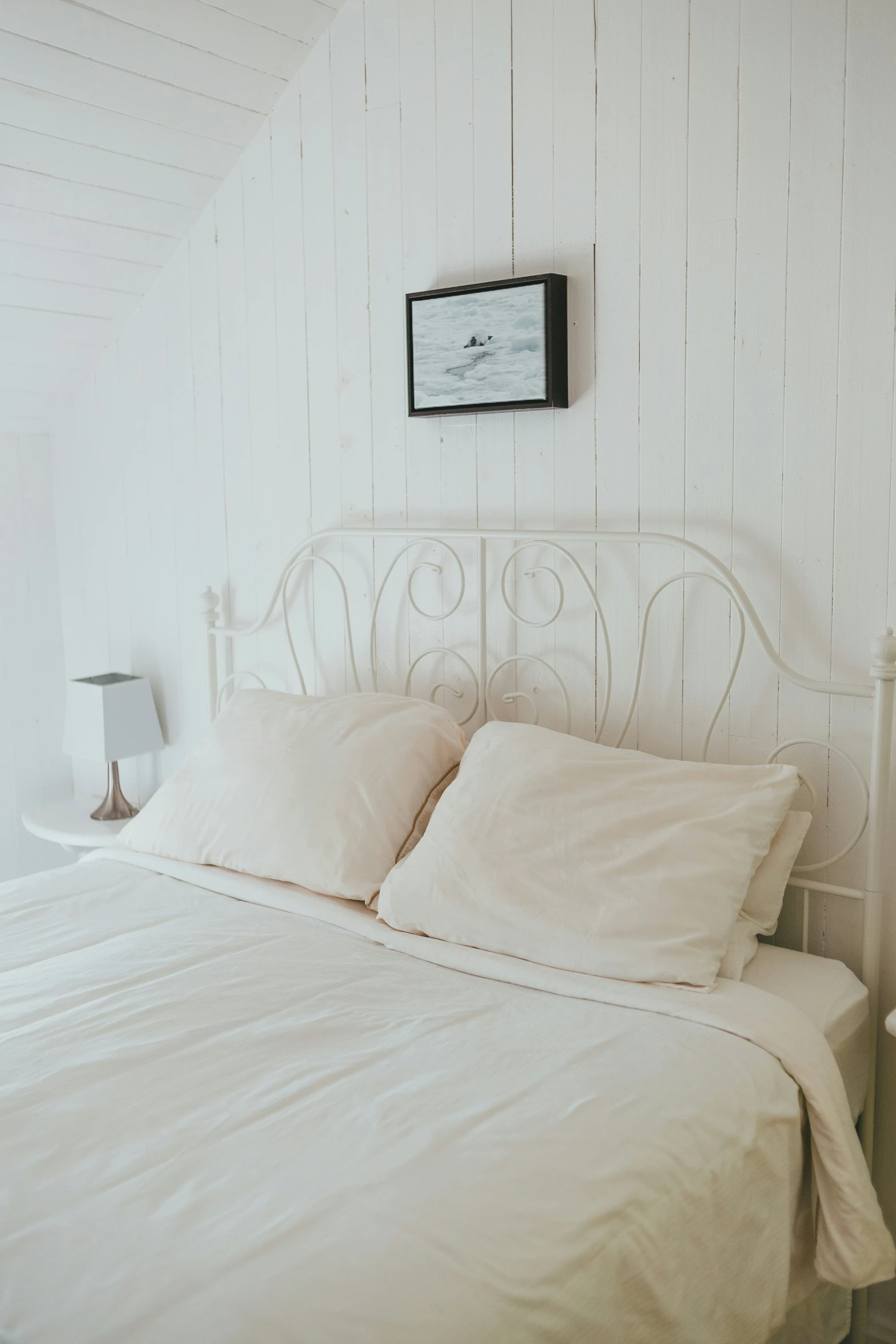 there is white bed with two pillows and a nightstand on either side