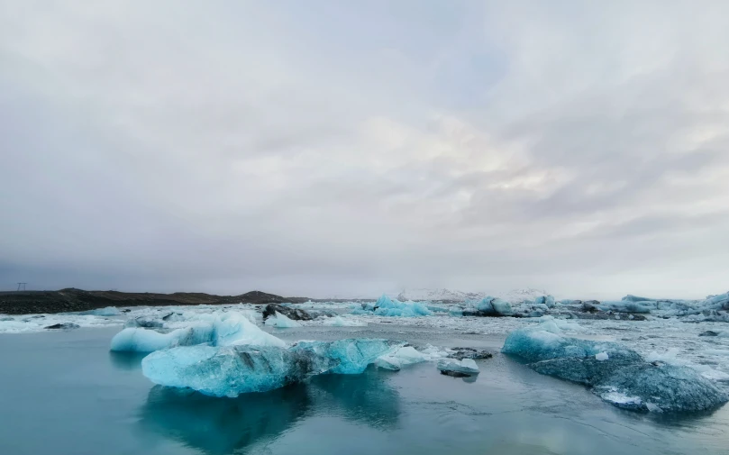 an icy lake surrounded by blue icebergs under a cloudy sky