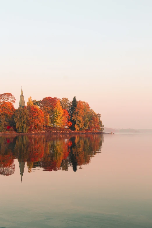 an island with trees in the foreground and lake, surrounded by bright autumn foliage