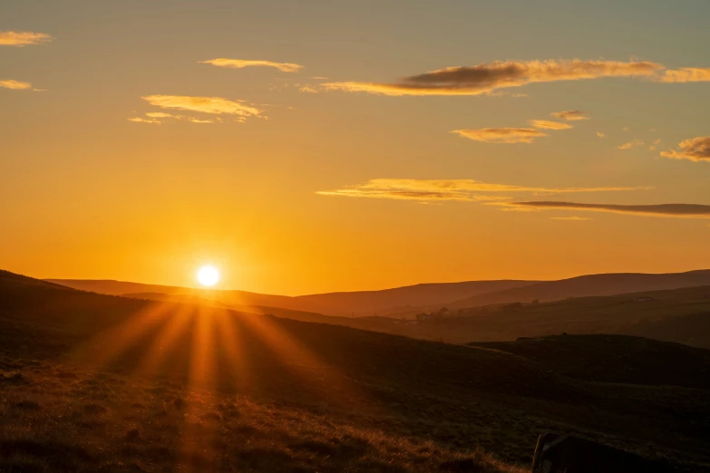 the sun sets over the hills with cows grazing