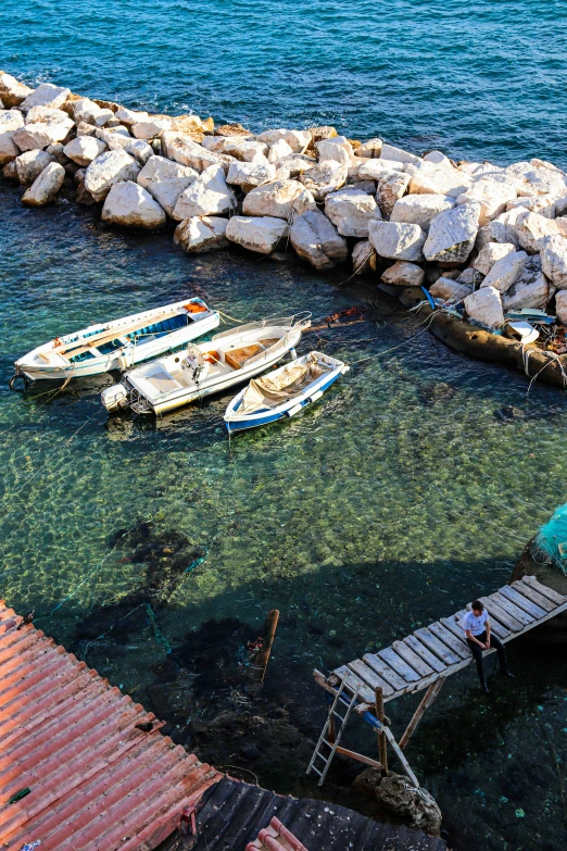 several small boats on water next to a rock wall