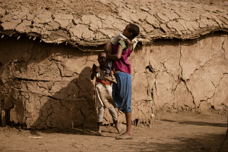 a woman is standing outside a mud hut with her baby