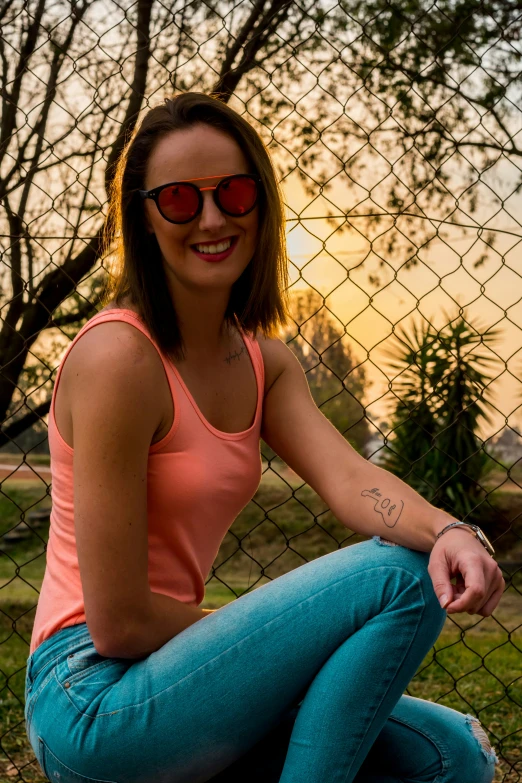 a girl sitting in front of a chain link fence posing