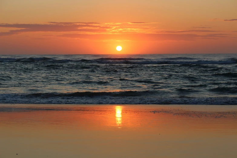 an ocean beach with waves on it and the sun going down