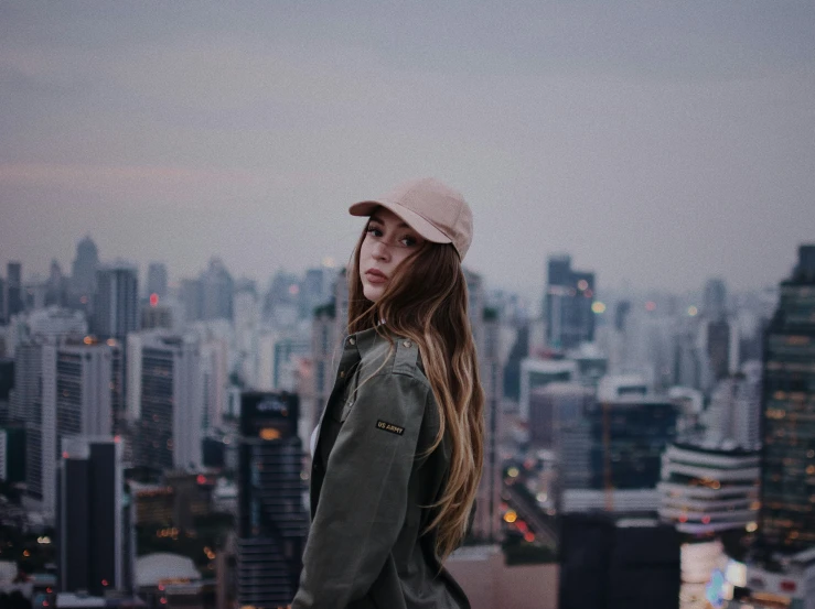 a beautiful young woman in a hat standing on top of a building