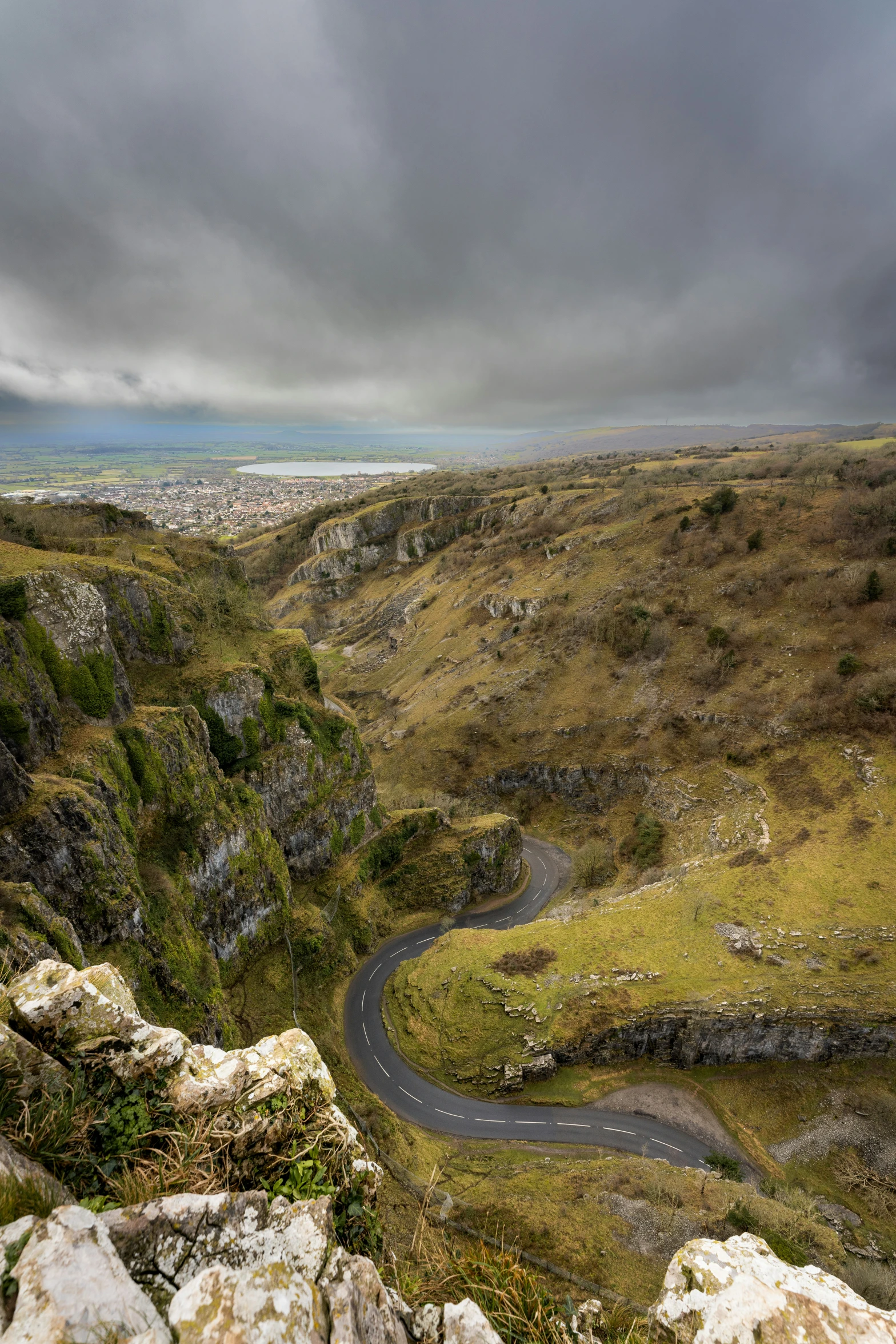 winding road in green mountainside with large grey clouds