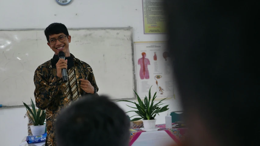 a man talking into a microphone in front of a class room