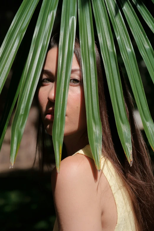 a woman standing under a palm leaf looking to the side