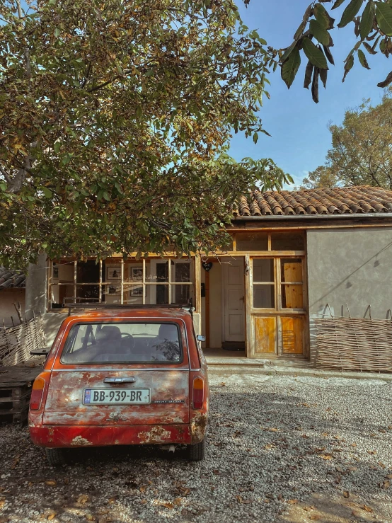 an old rusted car in front of a home with large windows