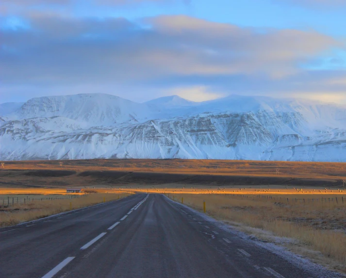 a road with a hill in the background and a snow covered mountain in the distance